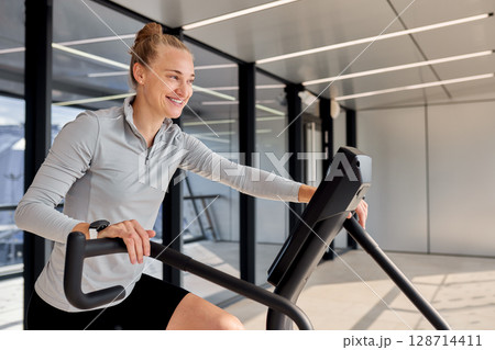 Woman exercising on a stationary bicycle in a modern fitness studio Woman exercising on a stationary bicycle in a modern fitness studio 128714411
