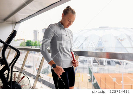 Woman preparing for a workout on a terrace near a sports complex Woman preparing for a workout on a terrace near a sports complex 128714412