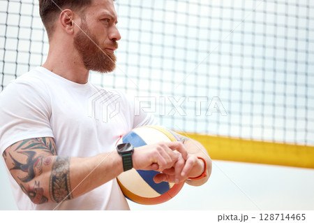 Athlete holding volleyball with net backdrop and focused expression outdoors 128714465