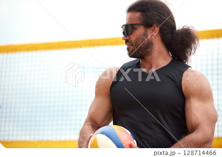 Man holding volleyball near net on a sunny outdoor beach court 128714466