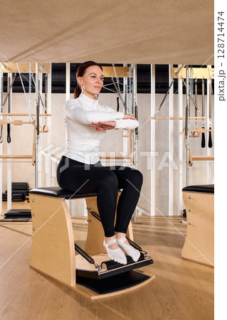 Woman practicing pilates exercise on reformer chair in modern fitness studio 128714474