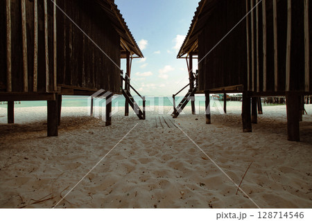Wooden huts on a sandy beach overlooking a calm ocean under a blue sky in Koh Rong Sanloem, Sihanoukville, Cambodia that shows the candid local daily island life Wooden huts on a sandy beach overlooking a calm ocean under a blue sky in Koh Rong Sanloem, Sihanoukville, Cambodia that shows the candid local daily island life 128714546