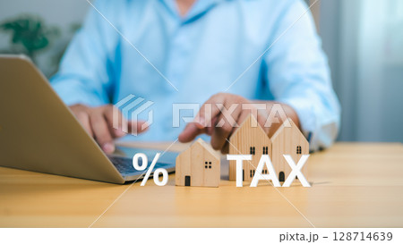 Tax property planning with a businessman using a laptop and wooden house models to represent real estate investment and financial calculation. Tax property planning with a businessman using a laptop and wooden house models to represent real estate investment and financial calculation. 128714639