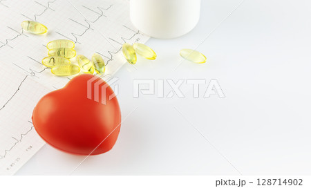 Vitamins and supplements for heart health. White bottle with healthy supplements in gel capsules, cardiogram and decorative heart on doctor desk with copy space. Omega 3 or vitamin D3 128714902