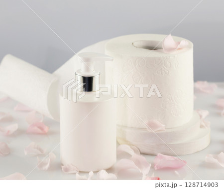 Roll of toilet paper with cosmetic dispenser bottle on light background with rose petals. White toilet tissue, Hygiene product. Restroom soft touch toilet paper. Soft focus style image Roll of toilet paper with cosmetic dispenser bottle on light background with rose petals. White toilet tissue, Hygiene product. Restroom soft touch toilet paper. Soft focus style image 128714903