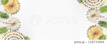 Holidays banner with holiday paper decoration and palm leaves on a white background with copy space. Party, carnival or festival background. Birthday or wedding concept. Flat lay, banner size Holidays banner with holiday paper decoration and palm leaves on a white background with copy space. Party, carnival or festival background. Birthday or wedding concept. Flat lay, banner size 128714904