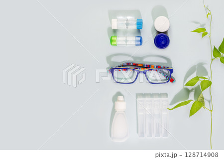Ophthalmology concept with kid eyeglasses, containers with contact lenses and moisturizing eye drops on blue background with copy space. Concept of eyecare, eye treatment and good vision. Flat lay 128714908
