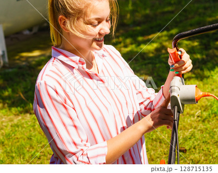Woman being mowing lawn with lawnmower 128715135