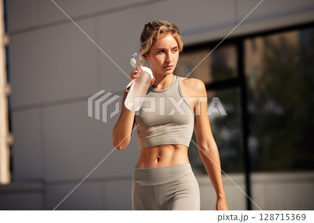 Athletic woman in sportswear outdoors carrying a water bottle after workout 128715369