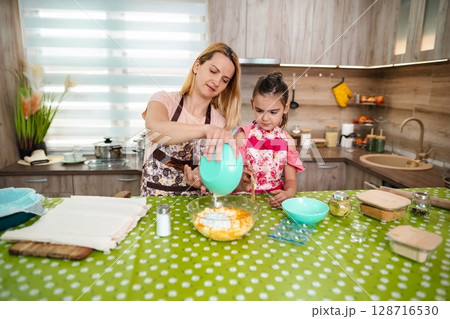 Mother and daughter baking together in a bright kitchen 128716530