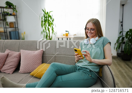 Relaxing at home with a smartphone and headphones in cozy atmosphere Relaxing at home with a smartphone and headphones in cozy atmosphere 128716571