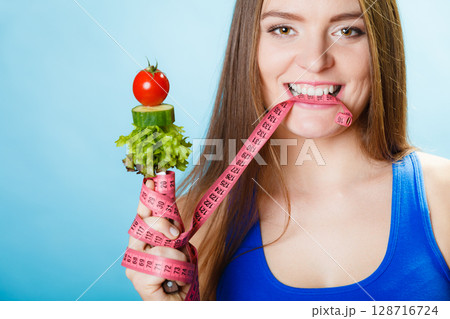 Woman biting measuring tape with vegetables. 128716724
