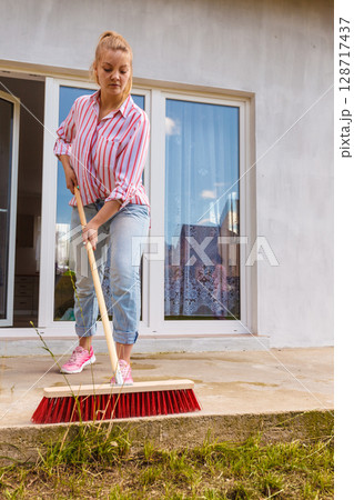 Woman cleaning patio using brush broom 128717437