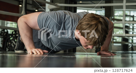 Young caucasian male person in gray sportswear doing press-ups or plank position look down at gym or fitness center. Low angle view. Close up 128717624