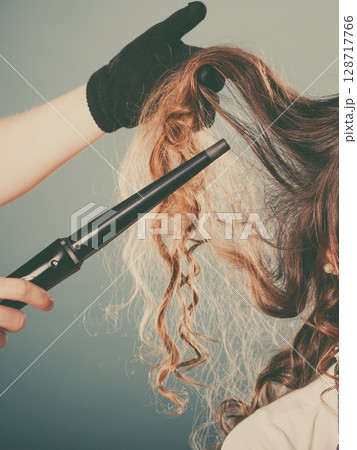 Hairdresser curling woman hair with iron curler. 128717766
