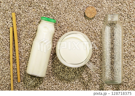Sunflower seed milk in glass cup and bottles on background with sunflower seed. Dairy free, non lactose, plant milk. Raw diet meal. Healthy vegetarian or vegan food. Eco friendly product. Flat lay 128718375