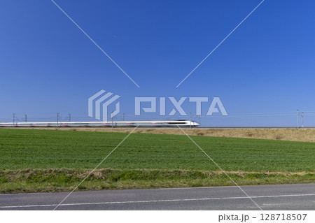 French TGV high speed train traveling through green field under blue sky French TGV high speed train traveling through green field under blue sky 128718507