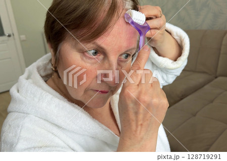 A beautiful senior woman is sitting at home and doing her make-up morning routine. Senior woman putting blush on her face 128719291