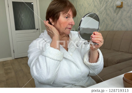 A refined senior lady is at her residence, carefully applying her makeup. A refined senior lady is at her residence, carefully applying her makeup. 128719313