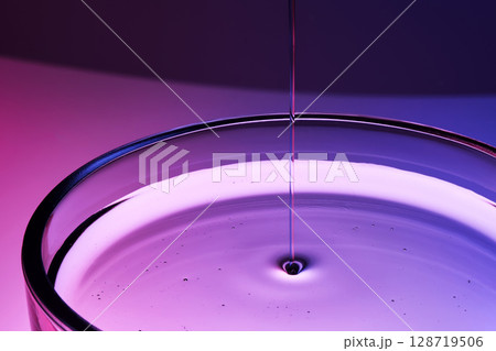 Serum or body cream flows into a petri dish on a purple background. 128719506