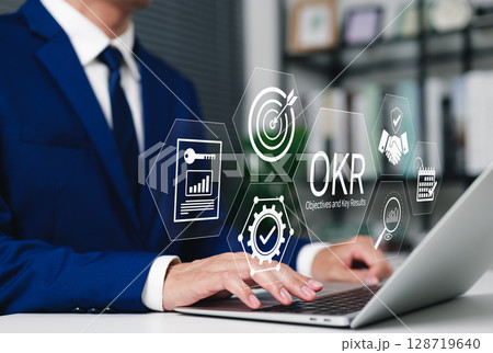 OKR Objectives and Key Results Business Strategy Concept. Businessman using laptop with OKR icons, target, charts, and gears, strategic planning, performance tracking, achieving corporate objectives, 128719640
