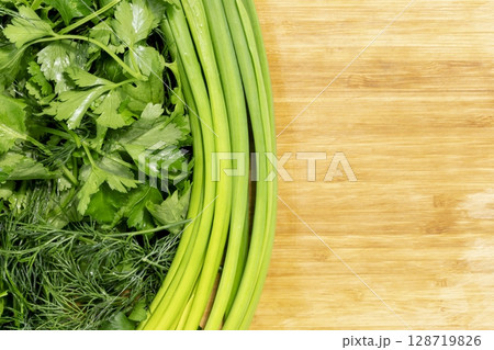 Fresh organic raw greenery. Parsley, dill, cilantro and green onion on wooden kitchen board with copy space. Vegan, vegetarian and healthy food concept. Closeup, flat lay 128719826