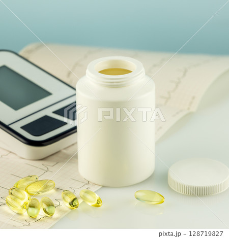 Mockup of natural vitamins or supplements, cardiogram and tonometer on doctor desk. White bottle with healthy supplements in gel capsules. Omega 3. Vitamins and nutrients for heart Mockup of natural vitamins or supplements, cardiogram and tonometer on doctor desk. White bottle with healthy supplements in gel capsules. Omega 3. Vitamins and nutrients for heart 128719827