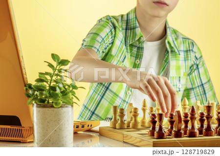 Child Learns how To Play Chess Through Internet. Boy, Teenager Play Chess Uses Laptop for Video Call. Remote Online Education, E-Education, Distance Learning, Home Education. Soft focus style image 128719829