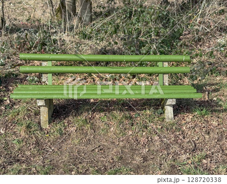 Green wooden bench in sunny park. Public space, relaxation area, and outdoor urban furniture 128720338