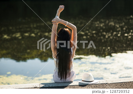 A girl sits on the shore of a lake A girl sits on the shore of a lake 128720352