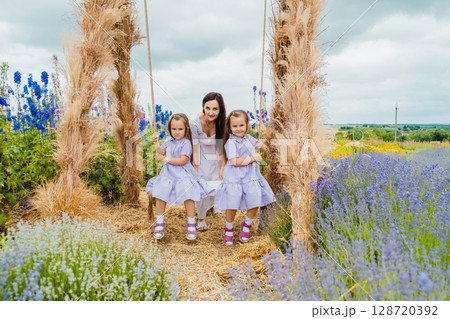 A young mother gently swings her twin daughters on a large, picturesque swing 128720392