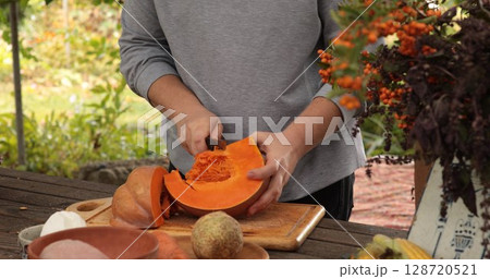 Preparation of fresh pumpkin for cooking on sunny day in outdoor kitchen with vibrant green background showcasing colorful plants and flowers 128720521