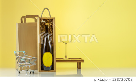 Eco friendly wine shop, wine bar winery or wine delivery concept. Mockup of bottle with champaign in a wooden box with wine glass, paper bag, shopping cart on yellow sunny background with copy space Eco friendly wine shop, wine bar winery or wine delivery concept. Mockup of bottle with champaign in a wooden box with wine glass, paper bag, shopping cart on yellow sunny background with copy space 128720708