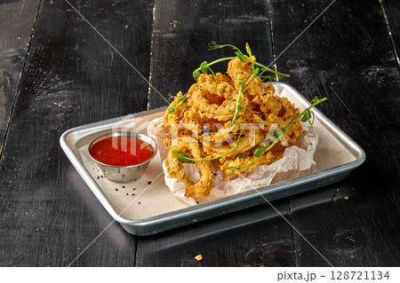 Deep fried onion rings with spicy sauce and pea sprouts on metal tray 128721134