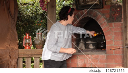 Preparation of flavorful dishes in outdoor kitchen with cooking oil added into pot situated in rustic setting surrounded by greenery, lanterns, and traditional accents enhancing ambiance 128721253