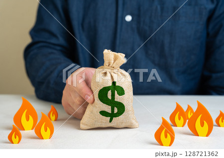 Dollar money bag surrounded by fire, concept. Save savings from depreciation, inflation and losses. Economic instability, hyperinflation risks, poor monetary policy, and loss of purchasing power. 128721362