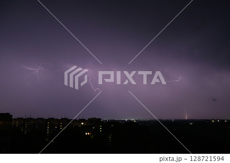Lightning flashing in distant stormy sky above city buildings. 128721594