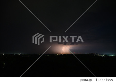 Lightning bolts and storm clouds over city during night. 128721599