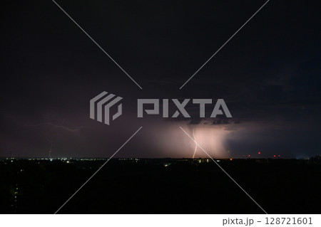 Lightning bolts and storm clouds over city during night. 128721601