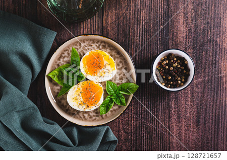 Soft-boiled egg split in half with spices and basil leaves on a plate on a table top view 128721657
