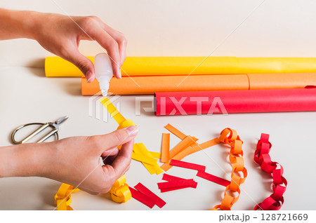 A girl's hands pour glue onto a strip of paper to make a paper chain A girl's hands pour glue onto a strip of paper to make a paper chain 128721669