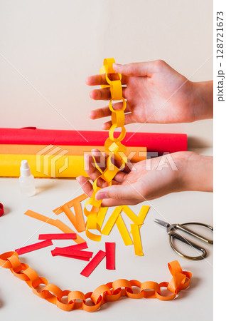 Handmade paper chain on women's palms and items for its production vertical view Handmade paper chain on women's palms and items for its production vertical view 128721673