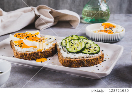 Open sandwiches with ricotta, cucumber and soft-boiled egg on a plate on a table Open sandwiches with ricotta, cucumber and soft-boiled egg on a plate on a table 128721680