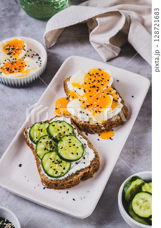 Cereal bread with cottage cheese, boiled egg and cucumber on a plate on the table vertical view Cereal bread with cottage cheese, boiled egg and cucumber on a plate on the table vertical view 128721683