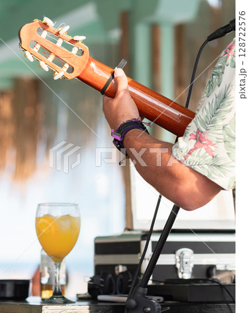 Musician playing guitar outdoors with tropical background and drink 128722576