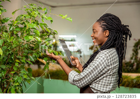 Flower shop assistant making pictures of plant and smiling Flower shop assistant making pictures of plant and smiling 128723835