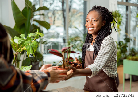 Flower shop assistant selling flower to the customer and smiling nicely Flower shop assistant selling flower to the customer and smiling nicely 128723843