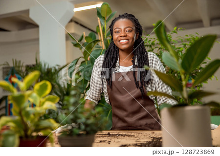 Cute african american woman in apron standing at the desk with plants 128723869