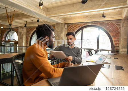 Colleagues working on a project and looking involved while discussing the details Colleagues working on a project and looking involved while discussing the details 128724233