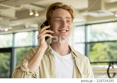 Smiling young man looking excited while talking on the phone 128724285